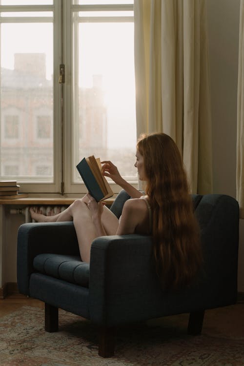 A Woman Reading a Book while Sitting on a Couch