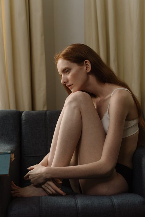 Free A contemplative woman sits in a moody, intimate indoor setting, exuding calmness and poise. Stock Photo