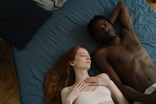 Free An interracial couple peacefully lying on a blue bed showing intimacy and relaxation. Stock Photo