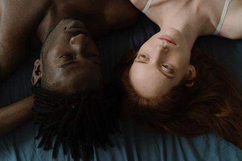 Free Top view of a serene interracial couple lying side by side on a bed, embracing love and intimacy. Stock Photo