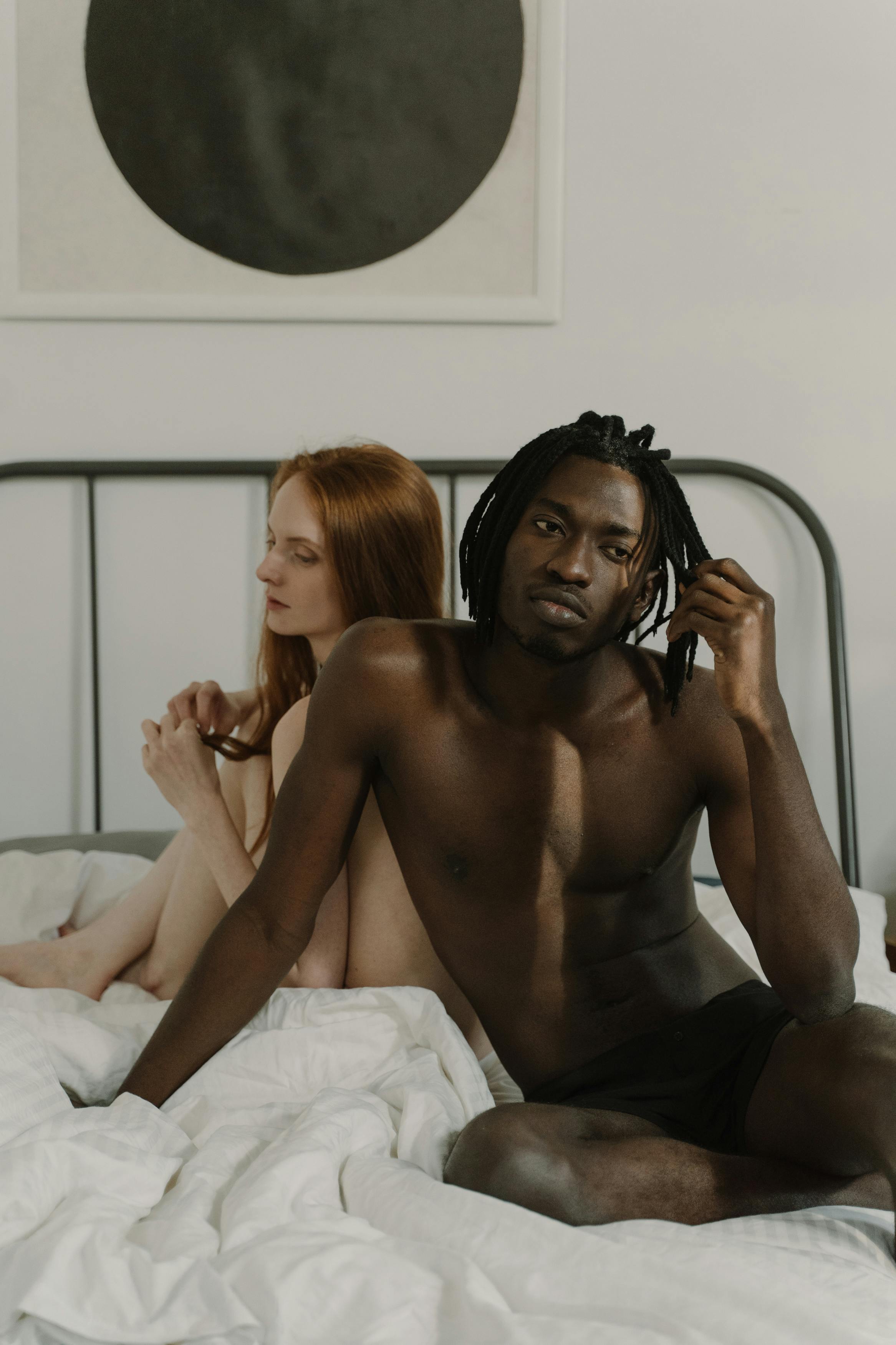 a shirtless couple sitting together on the bed