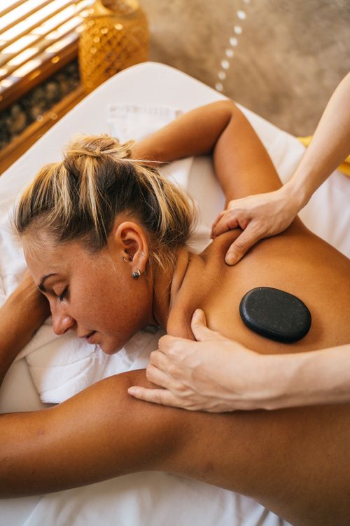 Free Woman enjoying a hot stone massage at a spa, promoting relaxation and pampering. Stock Photo