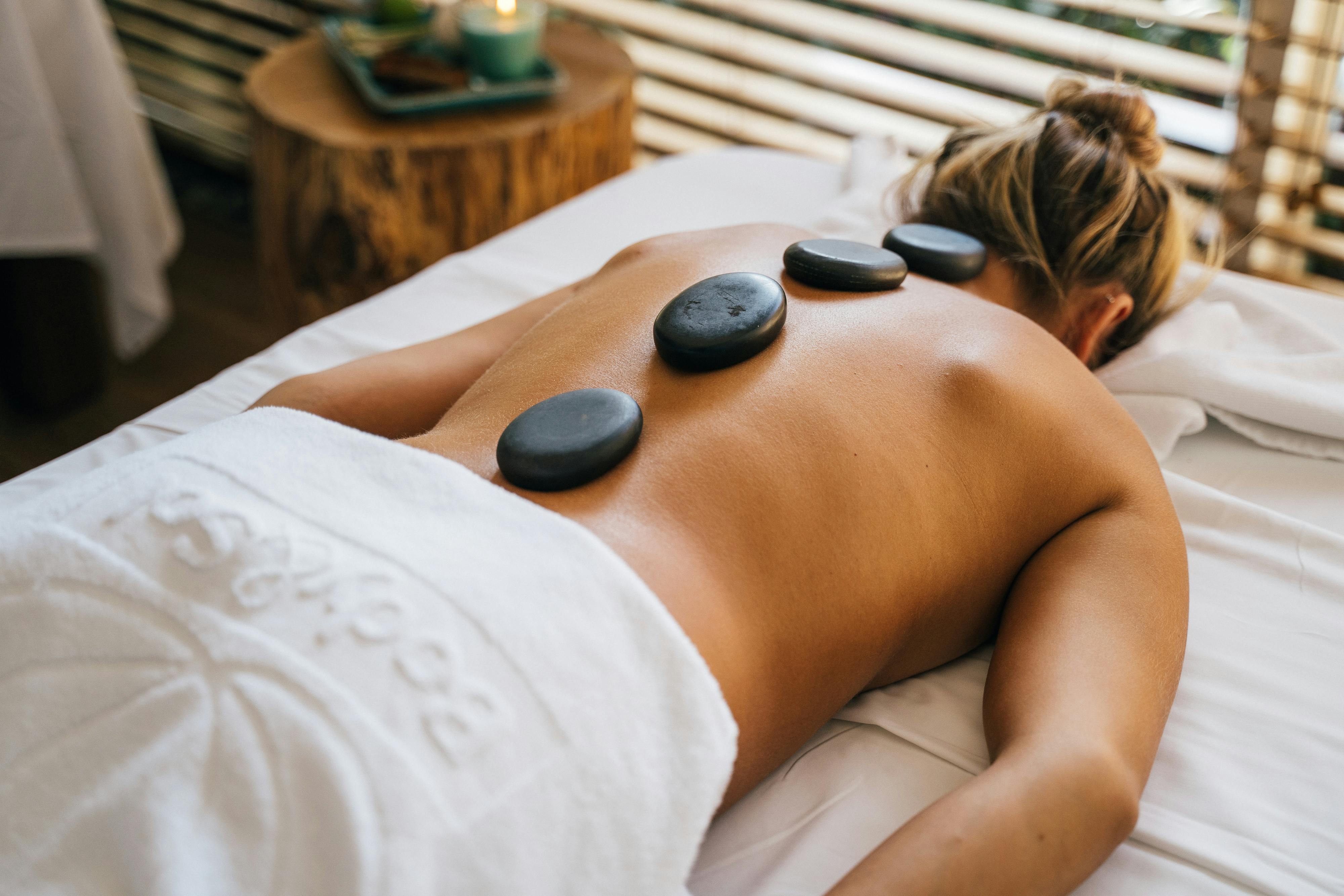 a topless woman lying down with basalt at her back