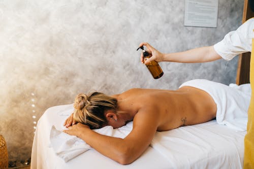 Free A Person Holding a Pump Bottle Near the Topless Woman Lying on Massage Table Stock Photo