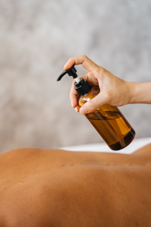 Free A Massage Therapist Putting Oil on a Client's Bare Back Stock Photo