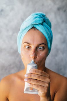 Woman with a towel headband holding a cream tube for facial care. Ideal for skincare themes.