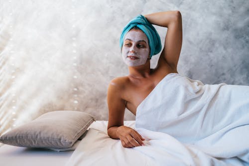 Woman Lying on Bed with Facial Mask and Blue Head Towel