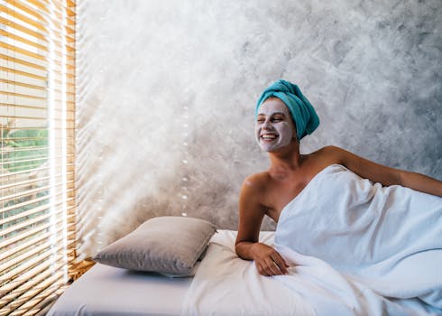 A woman enjoying a spa treatment with a facial mask, wrapped in a towel and smiling.