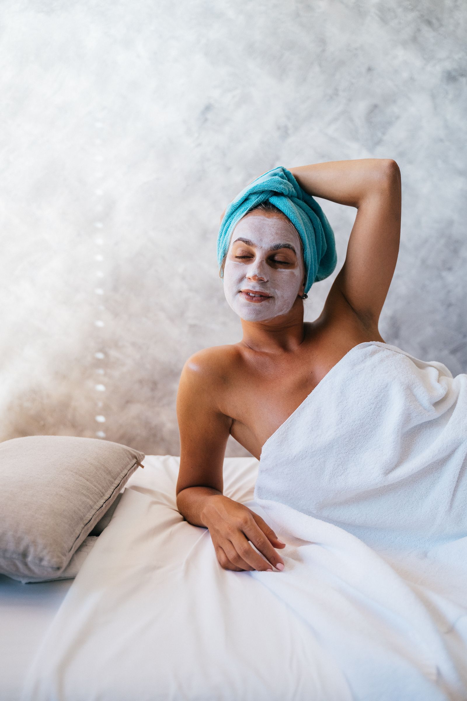 A woman relaxing in a towel wrap with a facial mask on, in a calm spa setting