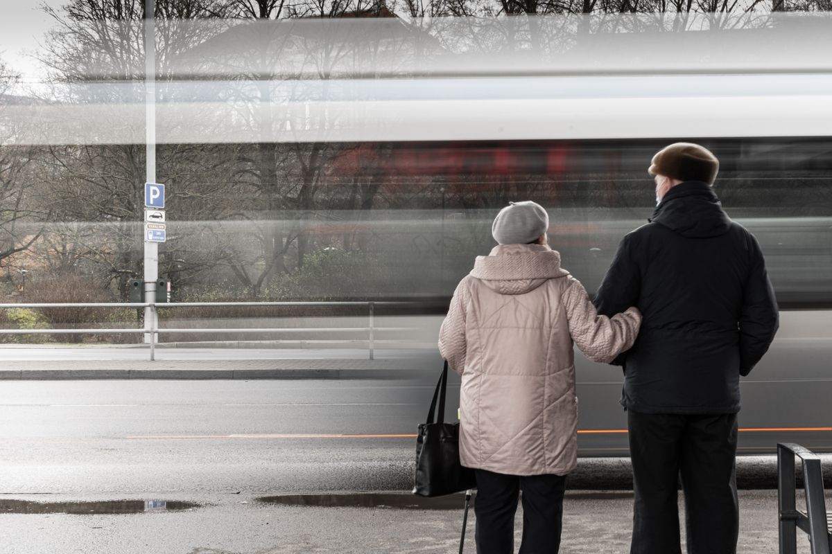 Casal de idosos esperando transporte em ponto de ônibus