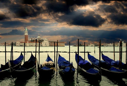 Gondolas resting at dawn with a dramatic Venetian skyline and cloudy sky in the background.
