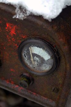 Close-up of a rusted vintage gauge with snow accumulation, showcasing decay and corrosion.
