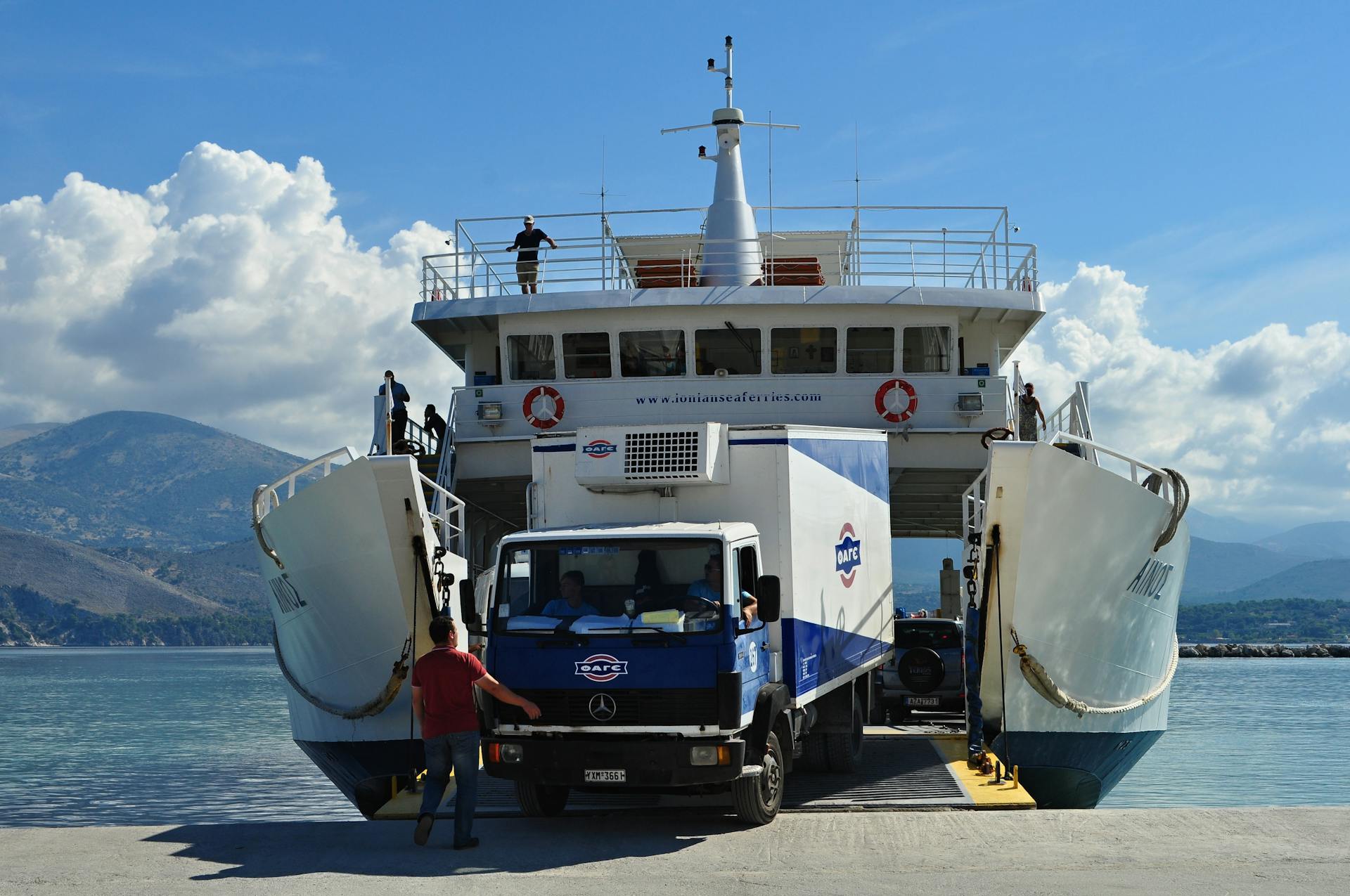 A ferry is being loaded with a truck at a harbor under a bright blue sky.