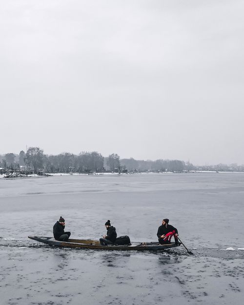 Free Three people paddling a wooden boat on a frozen Dal Lake in winter, Srinagar. Stock Photo