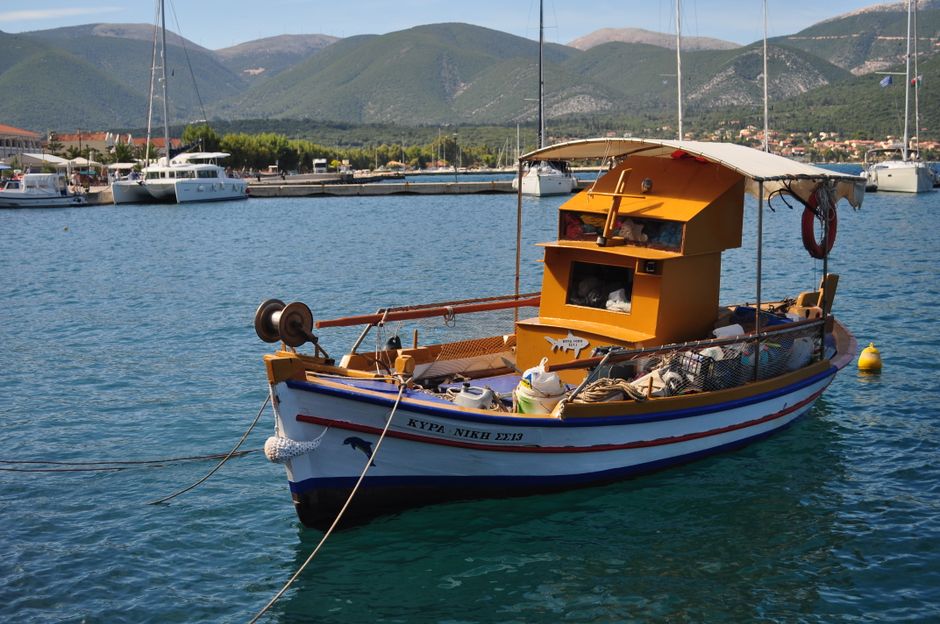 A traditional fishing boat moored in a calm harbor with scenic mountain backdrop.