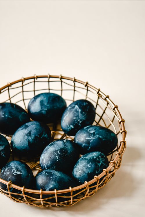 Free A basket of creatively dyed eggs on a textured surface, showcasing minimalist design and art. Stock Photo