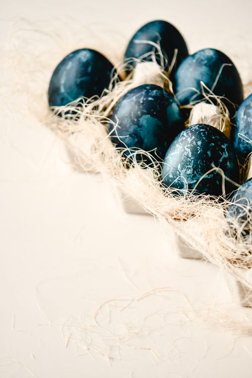 Free A minimalist display of blue dyed Easter eggs arranged in a straw-filled carton on a white surface. Stock Photo