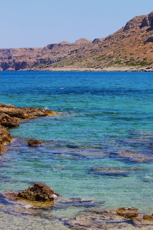 Free Stunning view of clear ocean water against a rocky coastal landscape under a blue sky. Stock Photo