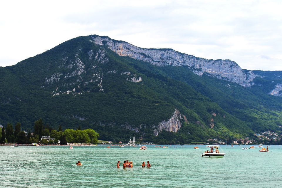 A tranquil lake scene with swimmers and boats against a majestic mountain backdrop, perfect for a summer retreat.