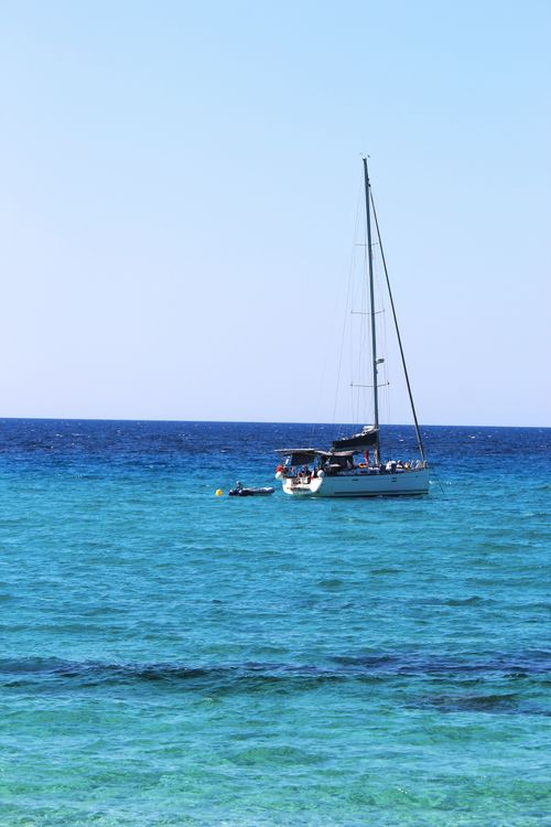 Free A serene view of a sailboat floating on clear blue ocean waters under a bright sky. Stock Photo