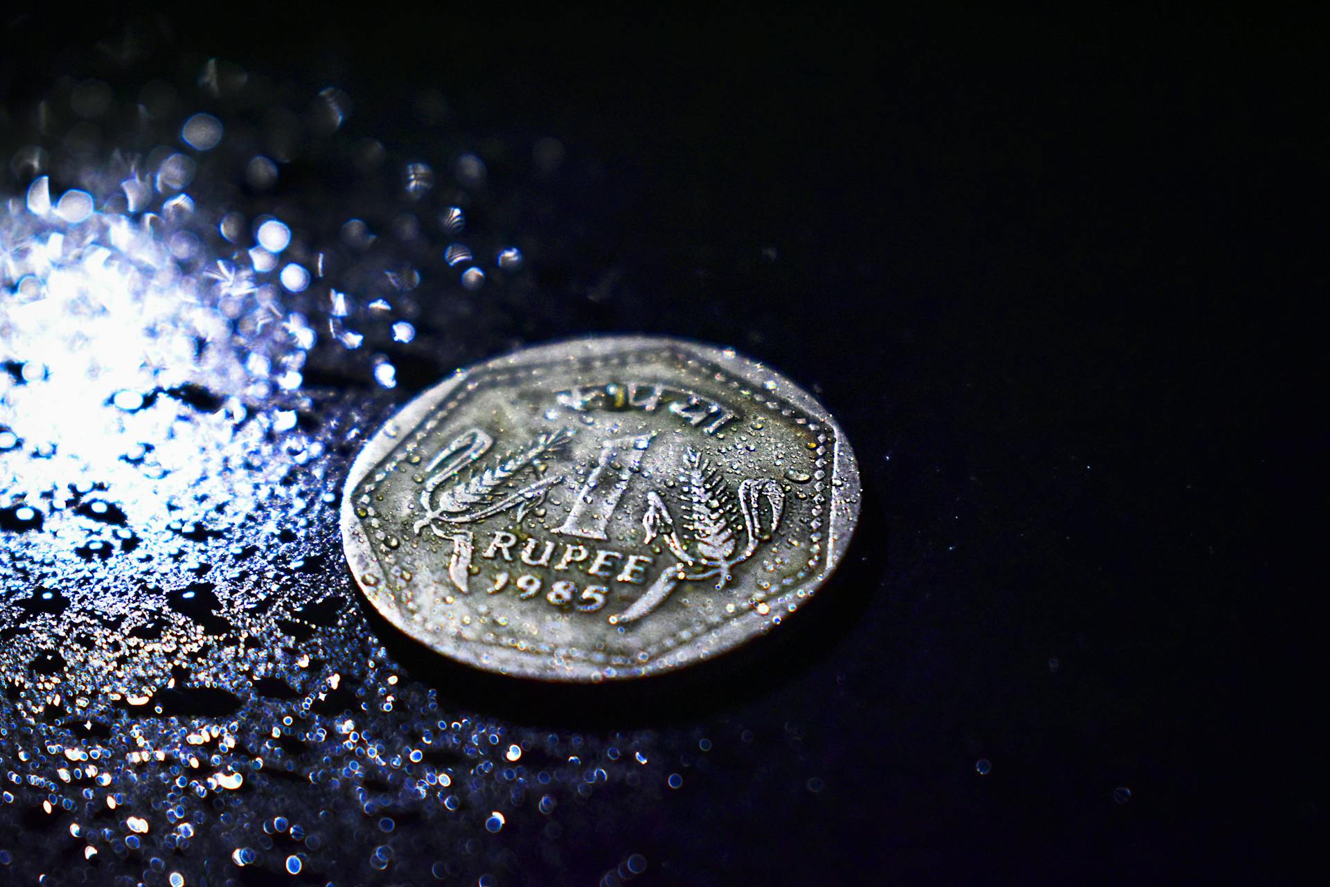 A detailed shot of a wet Indian rupee coin from 1985, highlighting texture and reflection.