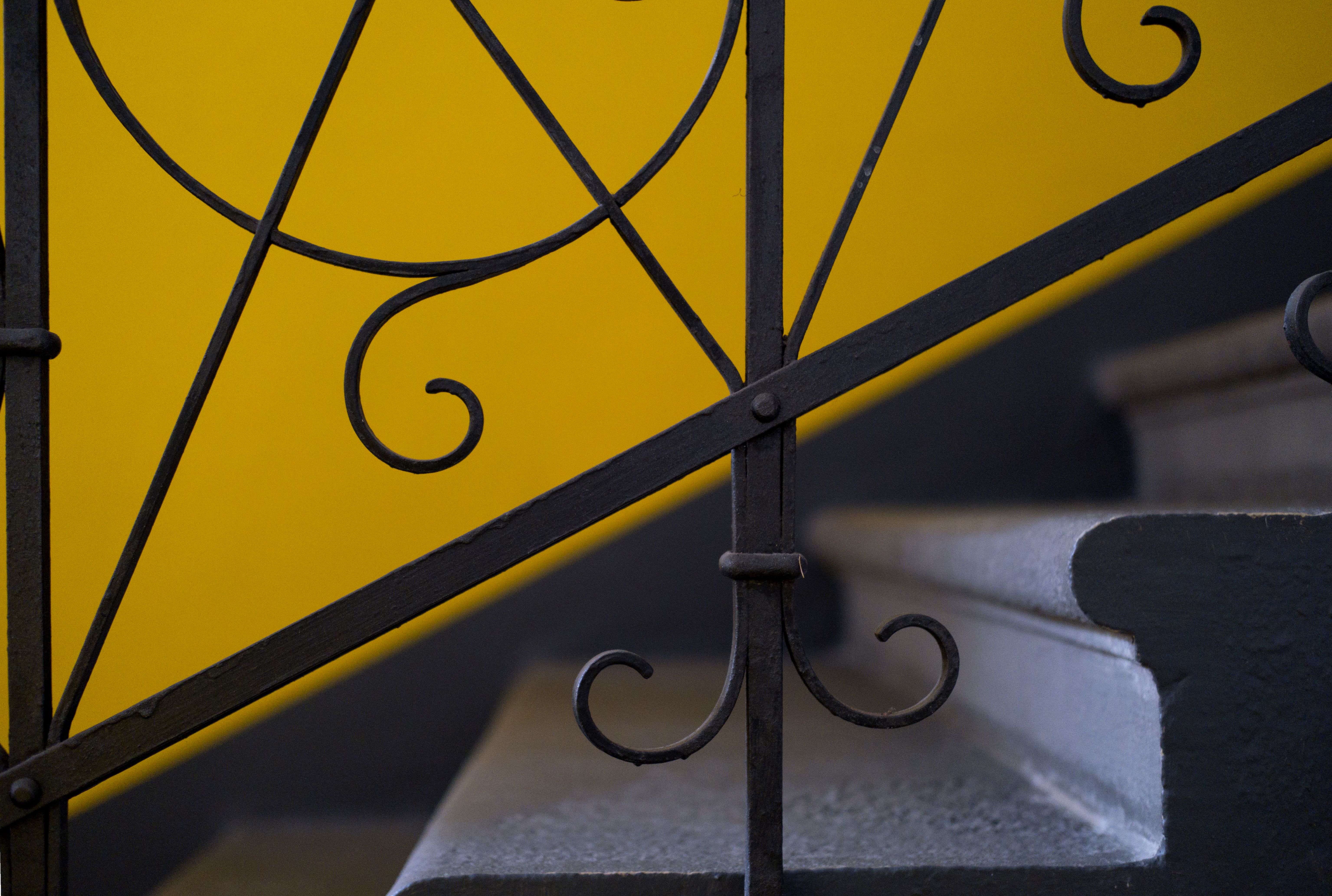 Close-up of a staircase with a yellow wall and decorative iron railing, perfect for design inspiration.