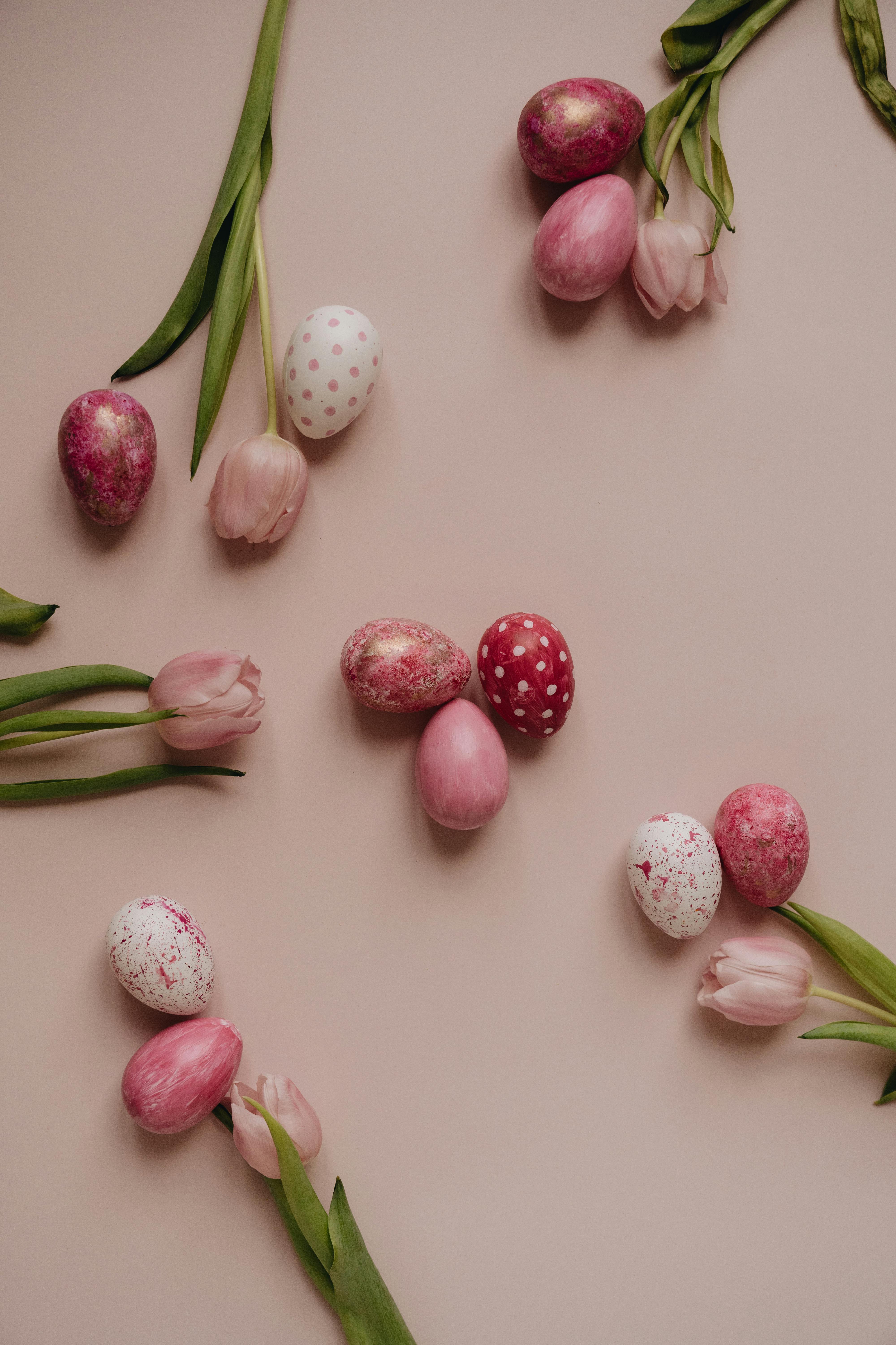 Aesthetic pink-themed flat lay with Easter eggs and tulips on a pastel surface.