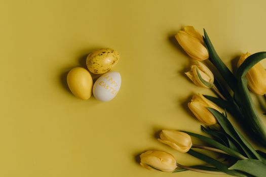 Flat lay of yellow tulips and Easter eggs on a yellow surface, perfect for spring and holiday decor concepts.