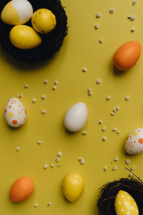 Free Scattered painted Easter eggs with small flowers on a vibrant yellow surface. Stock Photo