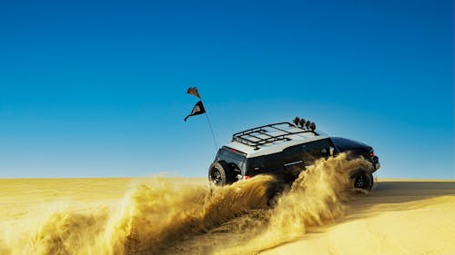 Free Modern off road car driving on sandy hill during road trip in desert valley under bright cloudless blue sky Stock Photo
