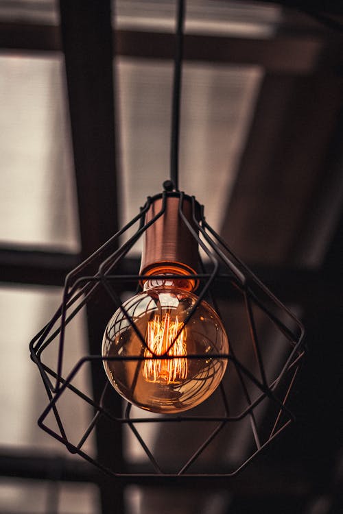 From below of shining bright glass lamp surrounded with steel geometrical construction and hanging on ceiling