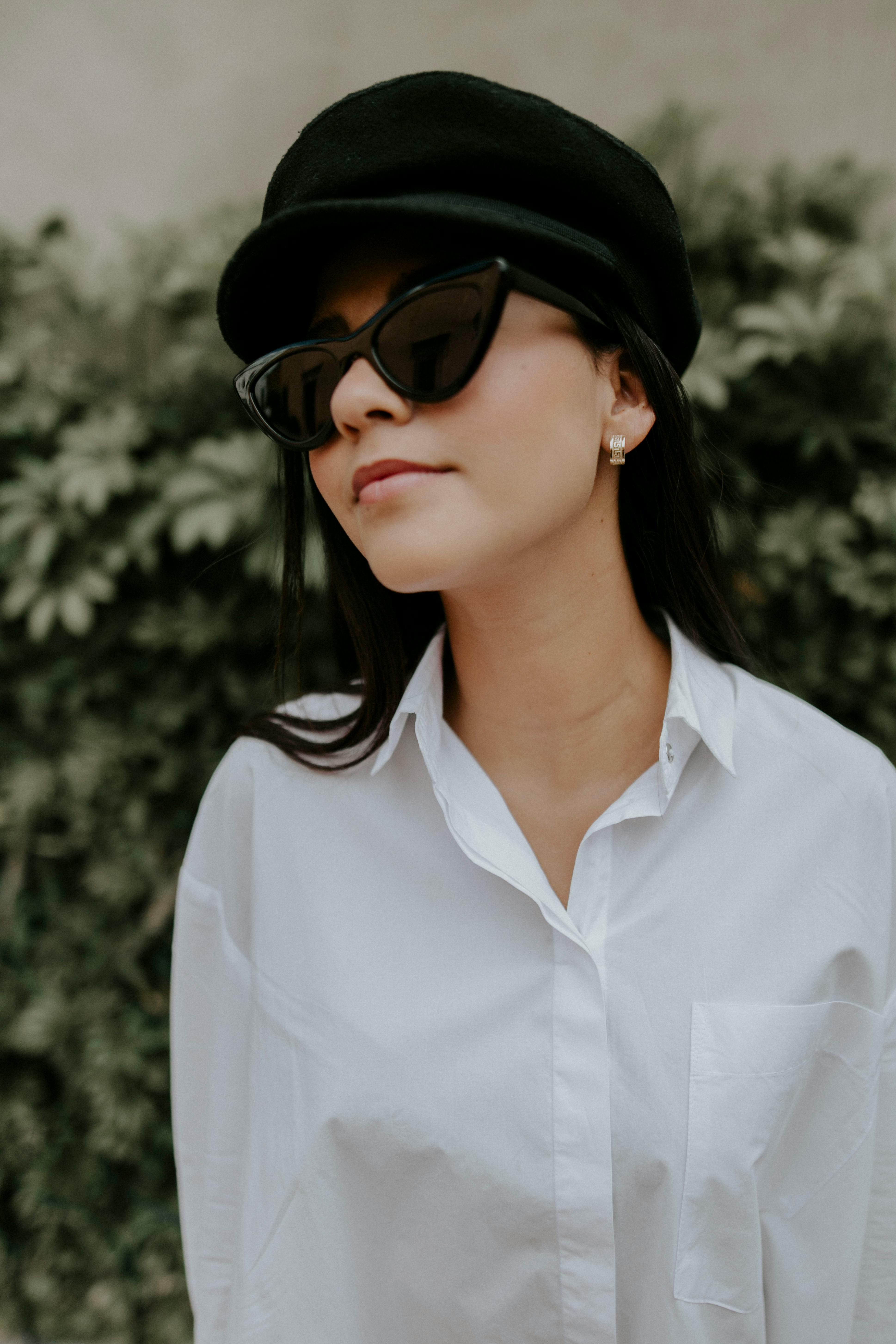 A fashionable woman in a white shirt and hat with sunglasses enjoying a day outdoors.