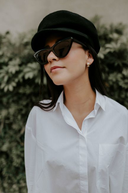 A fashionable woman in a white shirt and hat with sunglasses enjoying a day outdoors.