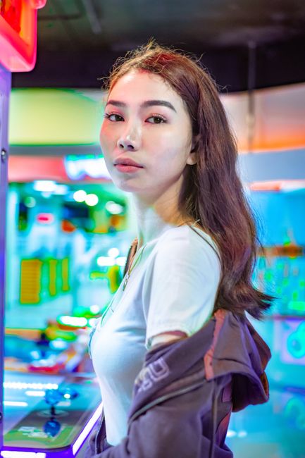 A fashionable woman posing confidently inside a vibrant amusement arcade setting.