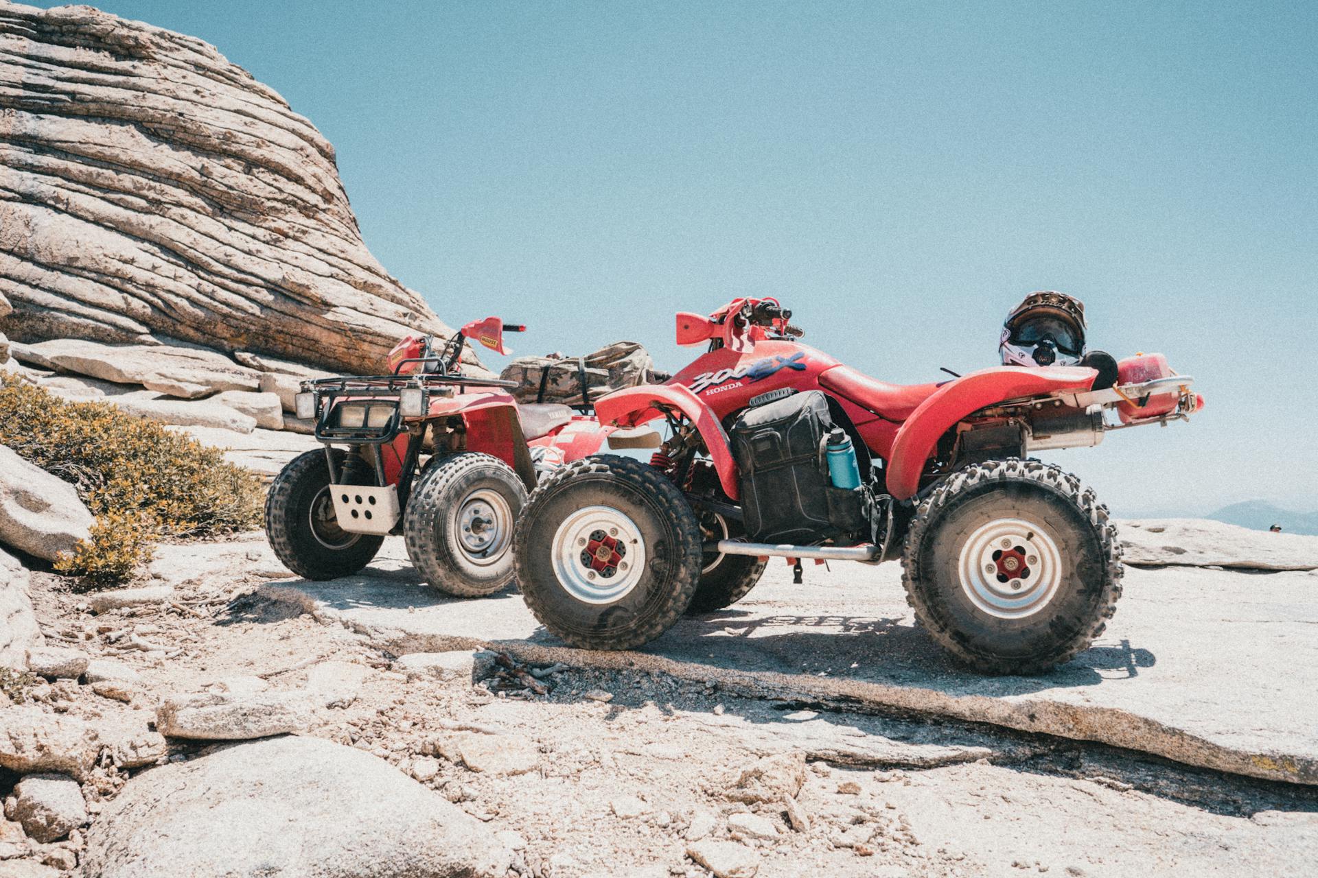 Red ATVs parked on rocky terrain at Bass Lake, CA under a clear blue sky.