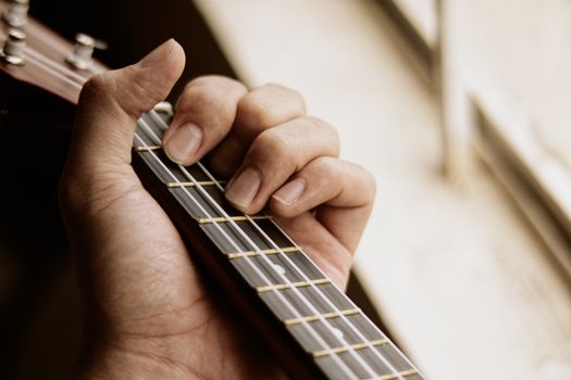 Crop anonymous male musician placing hand on acoustic guitar neck and playing music in light room