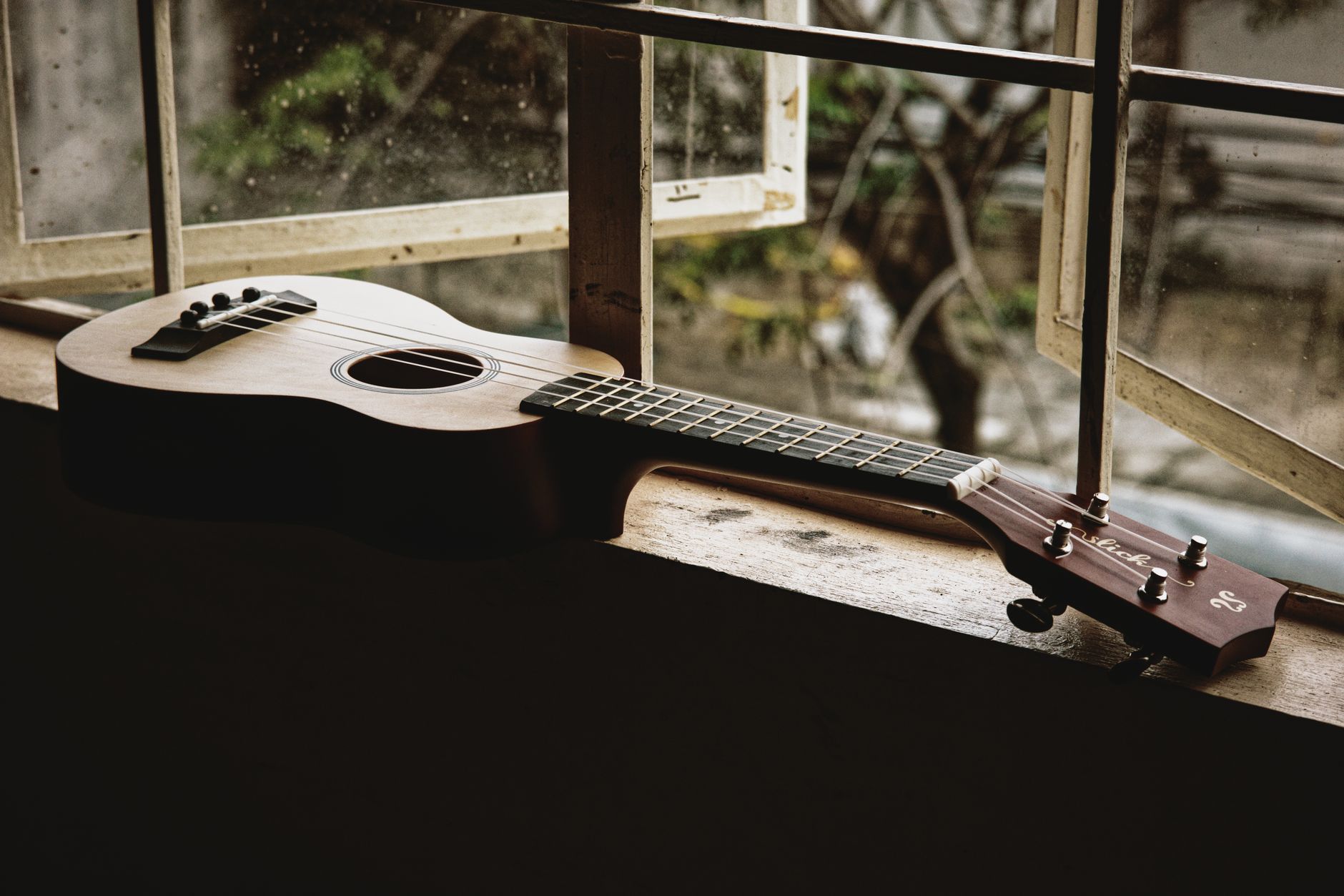 Classic acoustic ukulele placed on narrow windowsill of old rural house in daylight