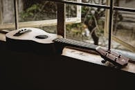 Classic acoustic ukulele placed on narrow windowsill of old rural house in daylight