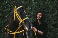 Cheerful ethnic man caressing young black horse