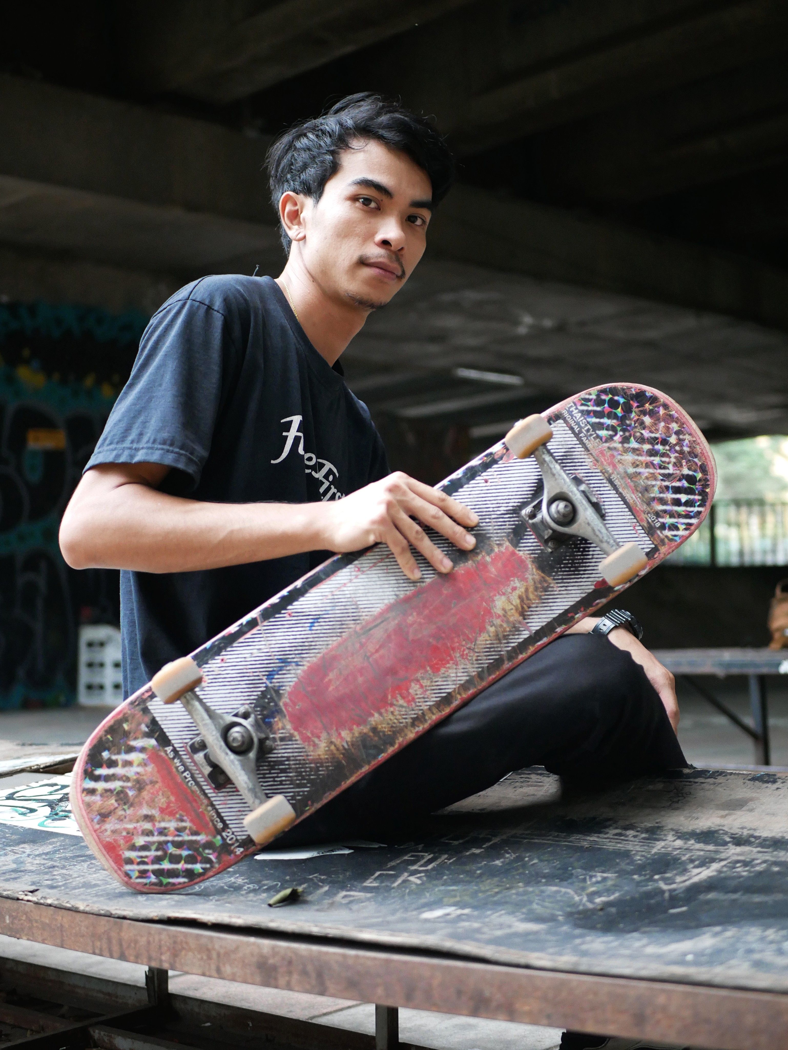Portrait of a young skateboarder holding a skateboard in an urban setting.