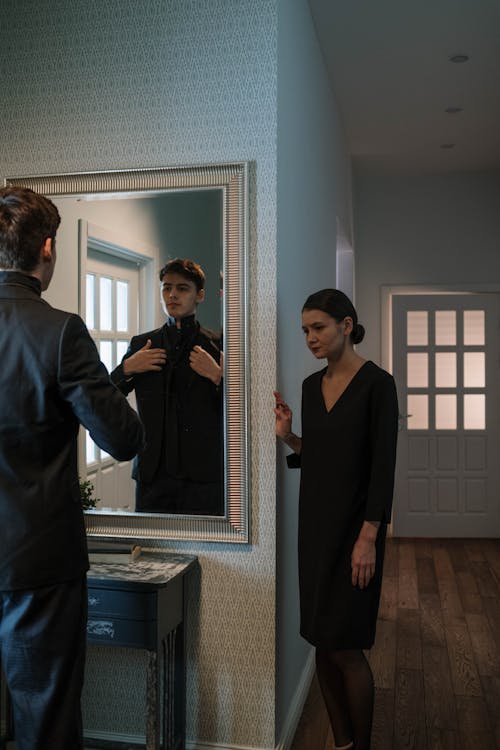 Woman Looking at her Boyfriend Getting Dressed Before a Mirror 
