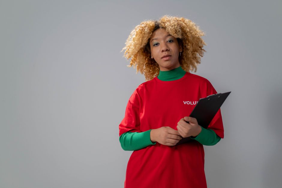 Portrait of a confident volunteer holding a clipboard in a studio setting with a neutral gray background.