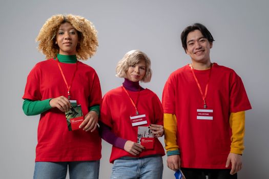 Three cheerful volunteers holding brochures and smiling at the camera.