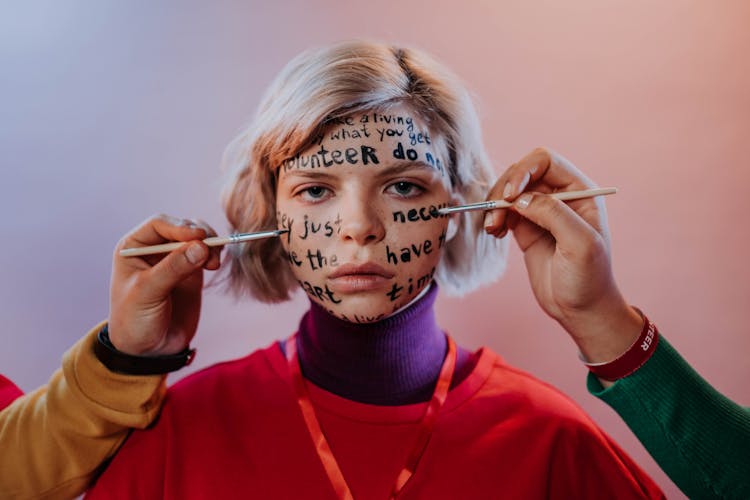 People Painting Words On A Young Woman's Face