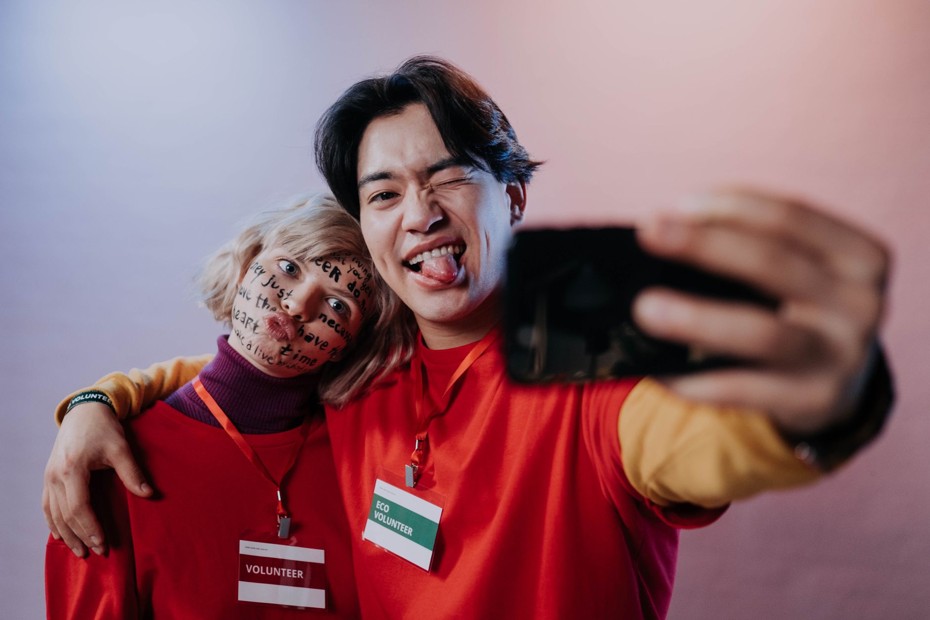 Two cheerful volunteers taking a playful selfie during a community service event indoors.