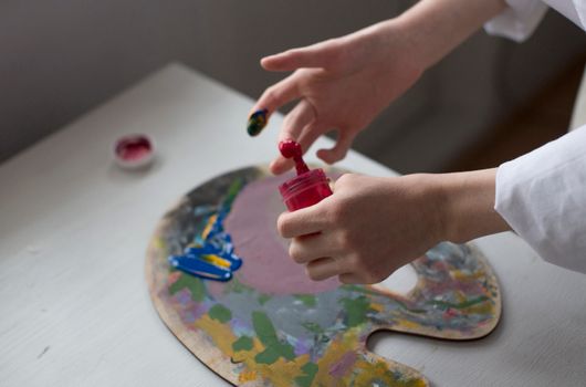 Close-up of an artist's hands mixing colorful paint on a palette indoors.