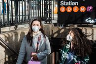 Multiracial female friends with shopping bag in protective masks walking up stairs of subway station on sunny street in city