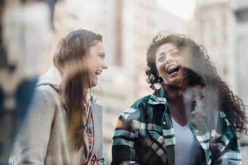 Free Through window of smiling multiracial female friends in outerwear having fun while standing near showcase on street on blurred background Stock Photo