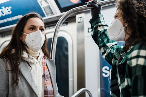 Content diverse female friends wearing outerwear in protective masks riding in subway train together during pandemic while commuting in metro