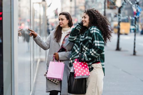 Free Side view of cheerful multiracial female friends with shopping bags standing on sidewalk near showcase of store on street on blurred background Stock Photo